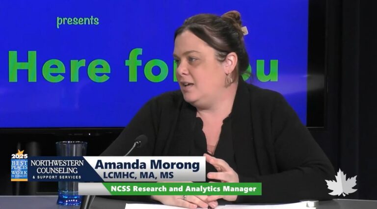 A woman with brown hair tied back, wearing a black top, speaks while seated at a desk. Text on screen reads “Amanda Morong, NCSS Research and Analytics Manager.” A Northwestern Counseling logo and “Here for you” appear in the background.