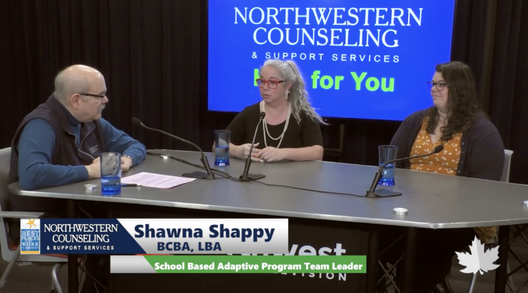 Three people sit at a studio table in discussion. Behind them is a screen displaying Northwestern Counseling & Support Services. A nameplate identifies Shawna Shappy as the School Based Adaptive Program Team Leader.